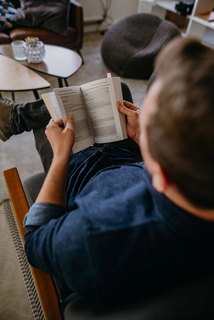 Ein Mann im blauen Hemd liest konzentriert ein Buch im Wohnzimmer