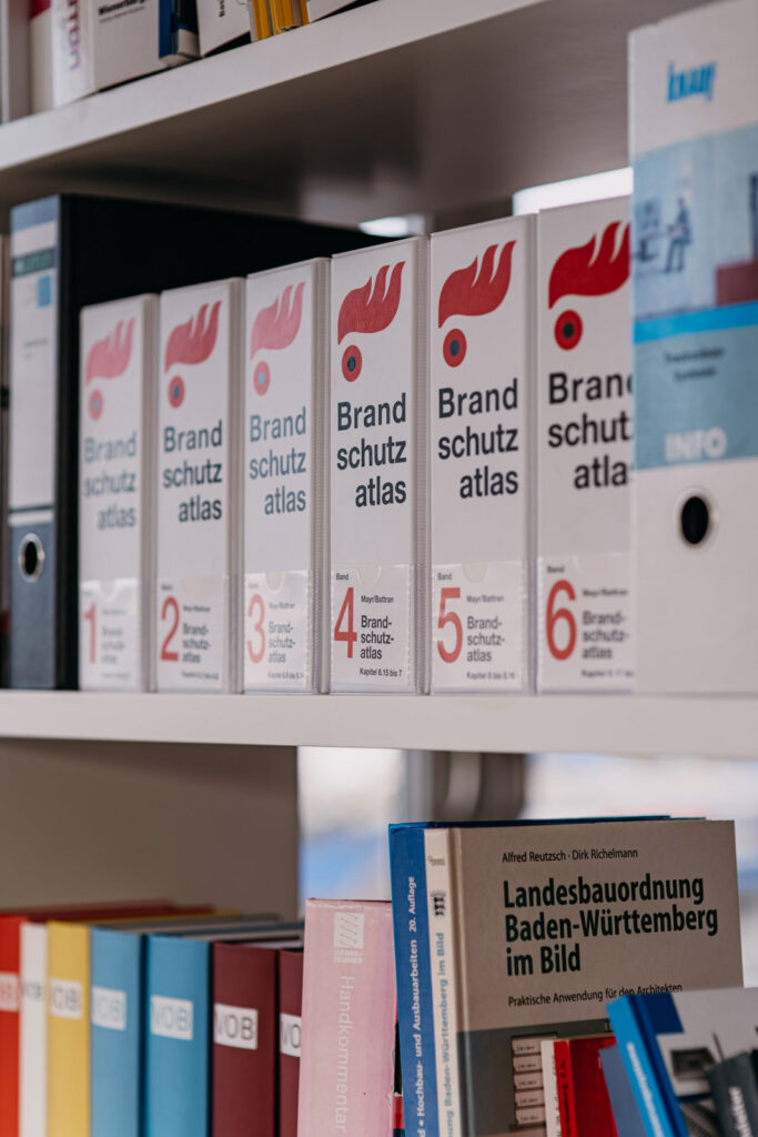 Regal mit sechs weissen Ordnern des Brandschutzatlas und Fachbuechern